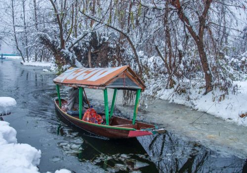 A tranquil scene of a wooden boat on a snowy canal in Kashmir, India.